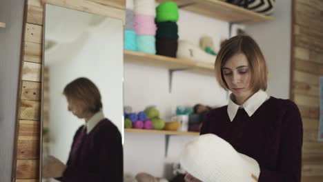 young woman standing front mirror with knitted cap. woman in textile workshop