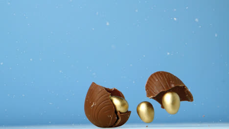 animation of chocolate easter egg falling and breaking open with gold eggs, on blue background