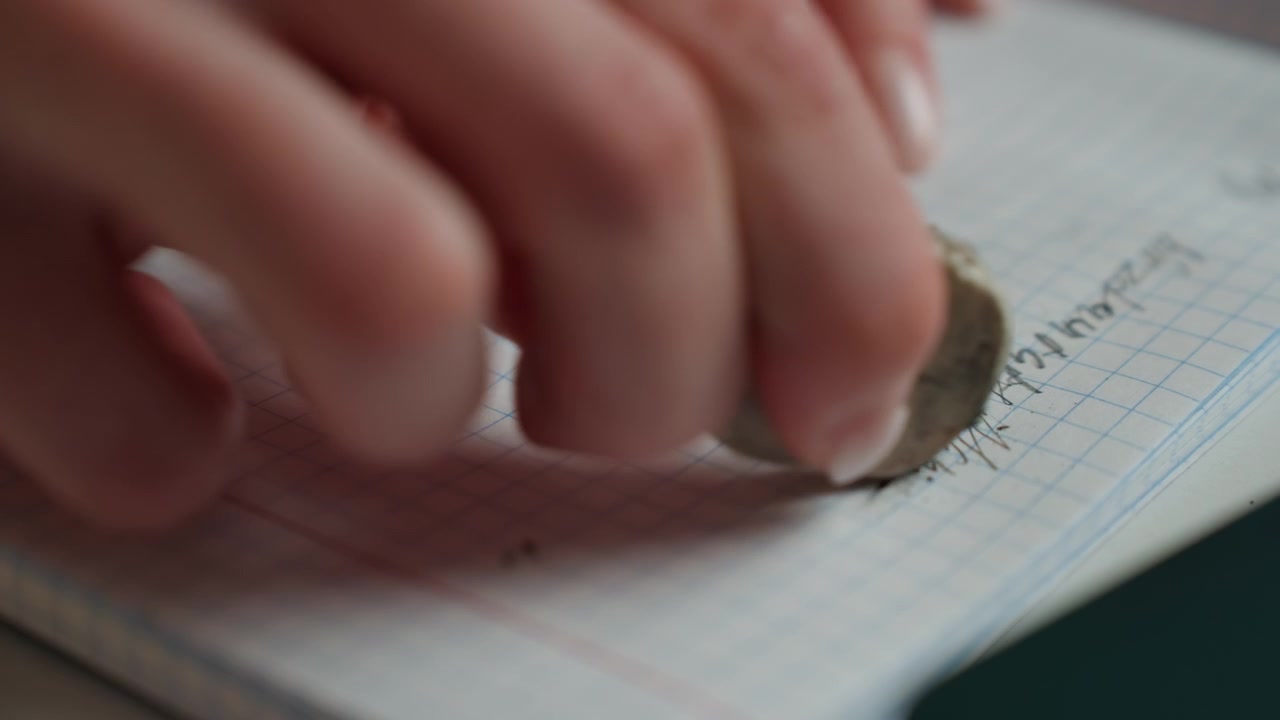 Hand clears lines on paper. Closeup of hand removing mistakes on notebook during calm tutoring. Woman carefully erases pencil errors on grid paper while concentrating during home learning