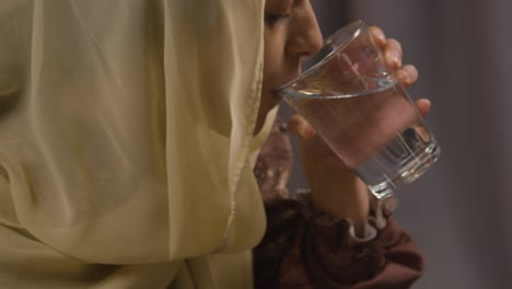 joven musulmana sentada alrededor de la mesa en casa bebiendo agua y comiendo dátiles celebrando eid