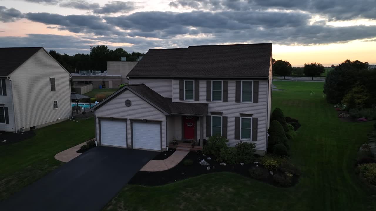 Aerial orbit shot of new modern single family house with double garage during sunset time. Swimming pool in backyard in new developed suburb housing area of United States.