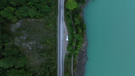 aerial view descending over camper van parked on the side of forest lake on a road trip