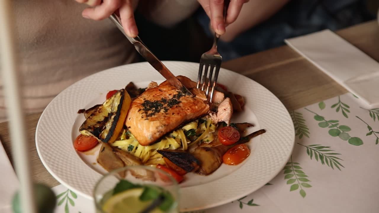 Primo piano di una persona che taglia un filetto di salmone con pasta e verdure
