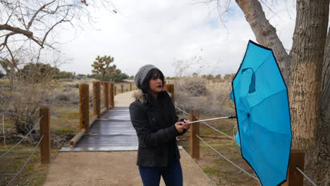 una hermosa joven abriendo un paraguas azul que se vuelve del revés mientras sonríe y se ríe en una tormenta de lluvia