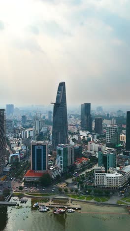 vertical drone shot of the modern skyline of ho chi minh city featuring the bitexco financial tower, viewed across the saigon river on a hazy afternoon. vietnam, uhd.