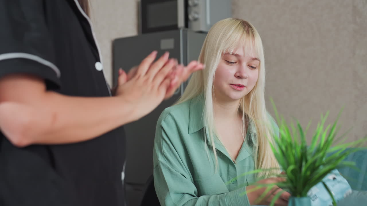 close up of young lady dusting her hand after eating cheese snack in kitchen, casual moment of wiping hands, friendly conversation in home environment, relaxed and natural interaction
