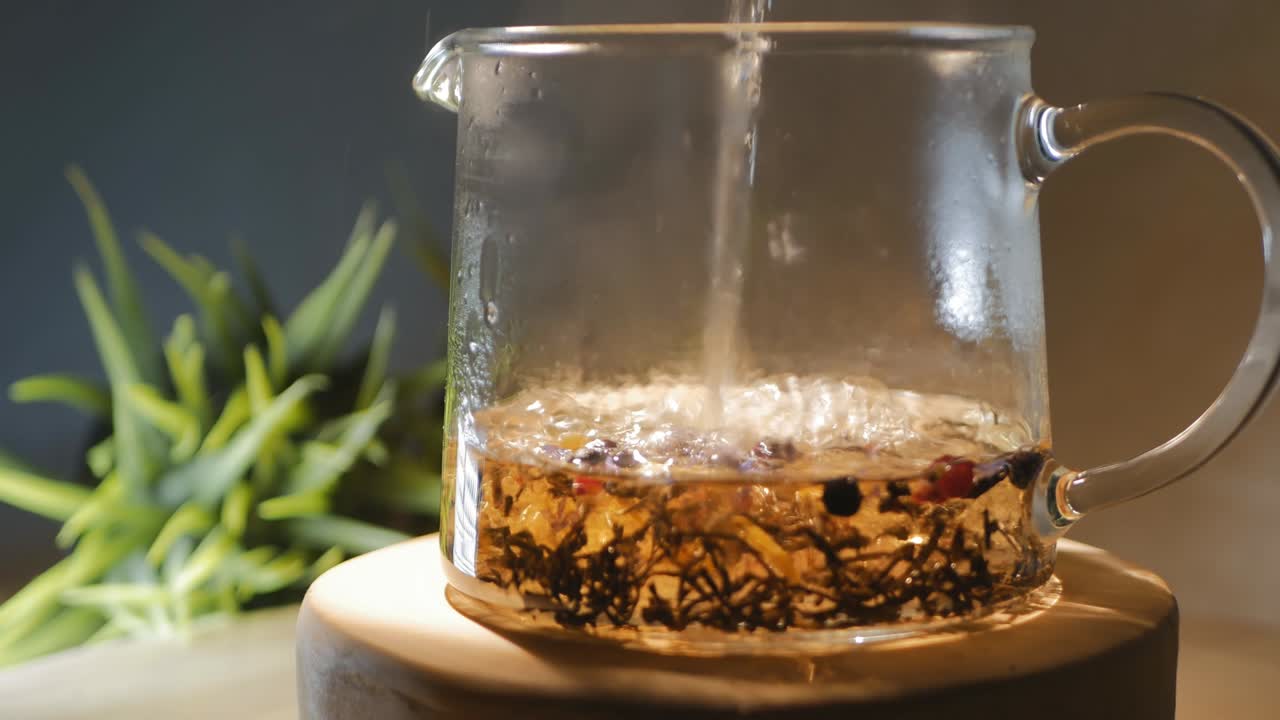 열매와 꽃잎을 가진 향기있는 허브 차는 투명한 유리 차 비에 부어집니다. 회전. 루프 비디오