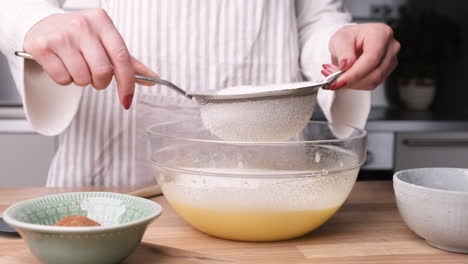 baker sifting flour on glass bowl with eggs for baking carrot cake