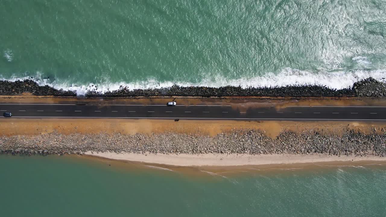 Top-down aerial drone shot of a road surrounded by the ocean, where tides gently spill over the edges of the path.