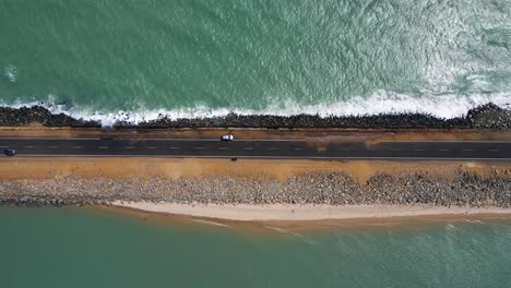 top-down aerial drone shot of a road surrounded by the ocean, where tides gently spill over the edges of the path.