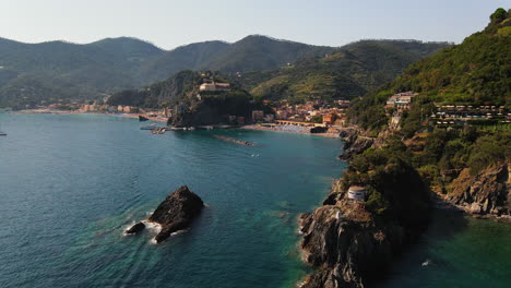 Aerial-view-of-cliff-with-greenery-and-small-house-and-resort-surrounded-by-sea-with-yachts-sailing-in-calm-and-silent-water-in-Portovenere-Village-in-Italy-during-day