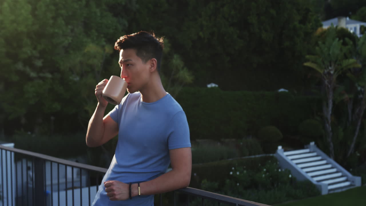 Asian man enjoying coffee on balcony, relaxing in peaceful garden setting, copy space