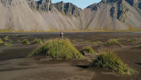 epic landscape in stokksnes. aerial drone circle movement around woman tourist on dune looking to the vestrahorn mountain. iceland nature.