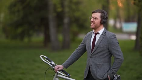 stylish young man in a business suit with a bicycle listening to music in headphones