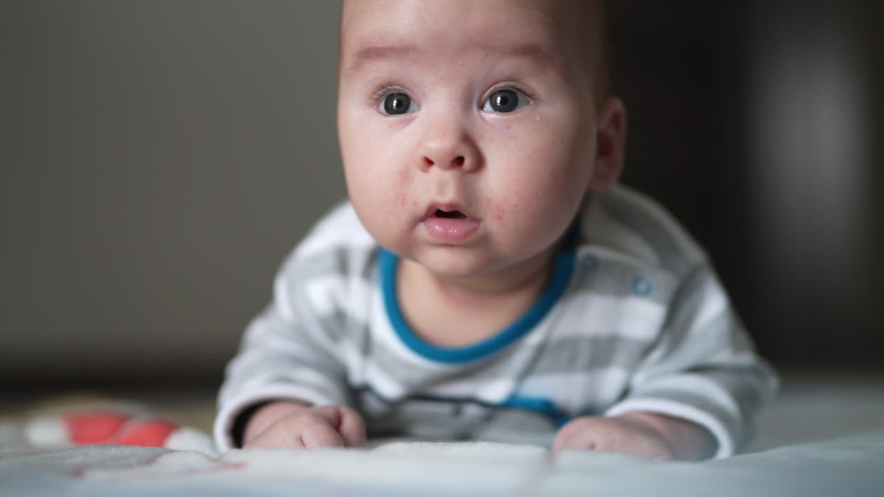 Interested look of a little toddler lying on his belly. Curious boy tries to keep his head and stares up. Close up.