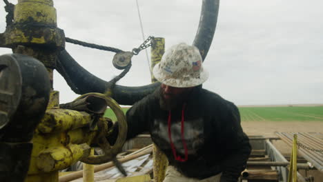 hard-working man wearing a helmet stands at the drilling equipment. worker turning the handle on the pipes.