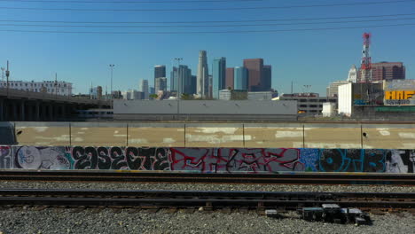Slow-aerial-push-over-train-tracks-in-an-industrial-area-of-Downtown-Los-Angeles-to-reveal-the-skyline-during-a-clear-day-Drone-California-USA