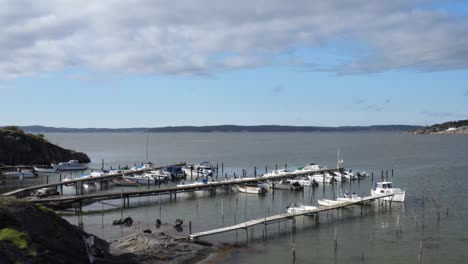 drone footage pushing forward of coastal island with green lush bushes summer day in aröd on the swedish west coast revealing boats and dock with the ocean in the background