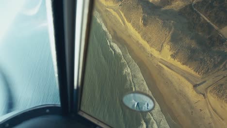 inside view from the cockpit of a flying moving plane flying over a beach with the ocean threw the window you can see the propellers of the plane on a beautiful sunny day in montalivet france