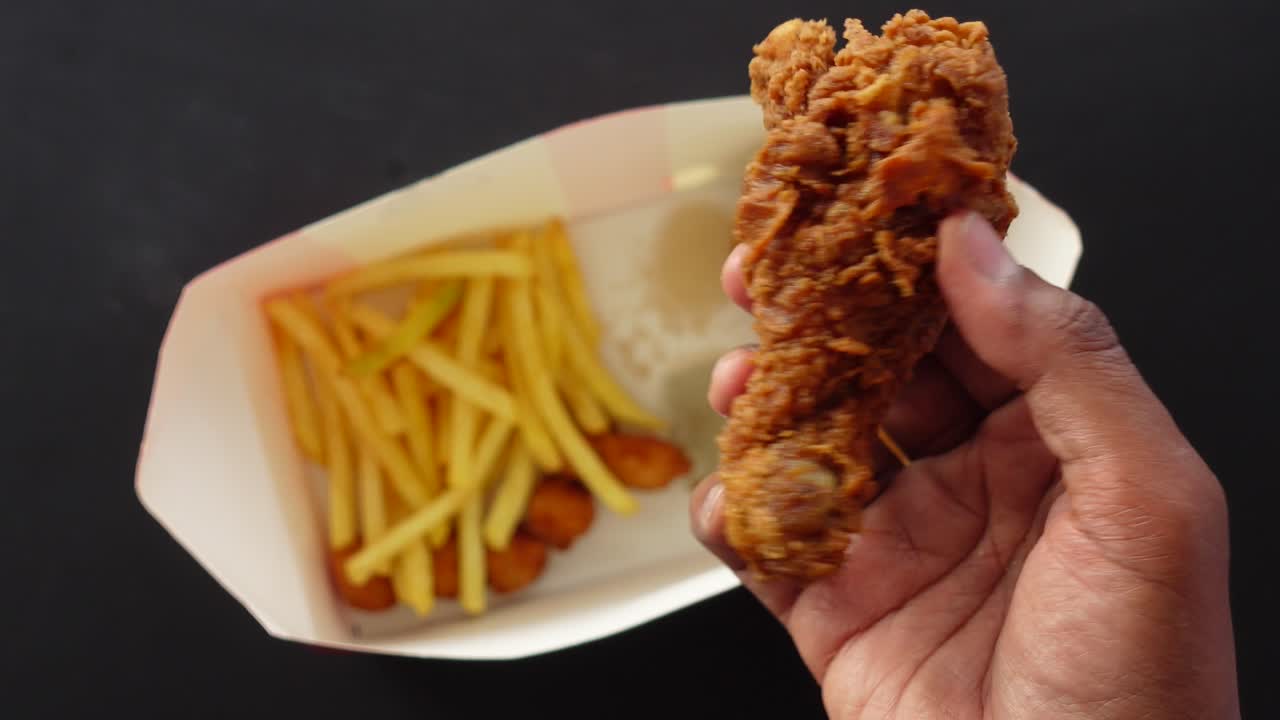 mano sosteniendo un pedazo de pollo frito crujiente con papas fritas