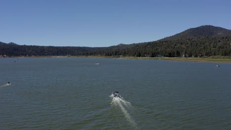 Aerial-drone-shot-following-a-white-boat-in-Big-Bear-Lake-in-San-Bernardino-County,-California