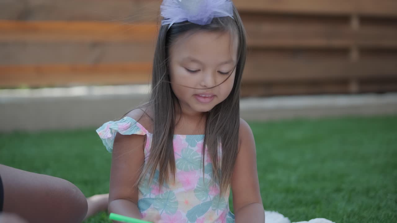 una madre y su hija pequeña se sientan en una manta en el patio trasero, participando en una actividad de dibujo juntos. la escena al aire libre captura un momento familiar pacífico, fomentando la creatividad y el vínculo.