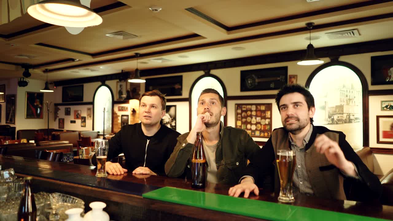 친구들은 스포츠 바에서 경쟁을 지켜보고, 그 다음에는 하이파이브를 하고 맥주를 마시며 승리를 축하합니다. 젊은이들은 긴장하고 행복합니다. 스포츠 팬들은 술집 컨셉에서 환호합니다.