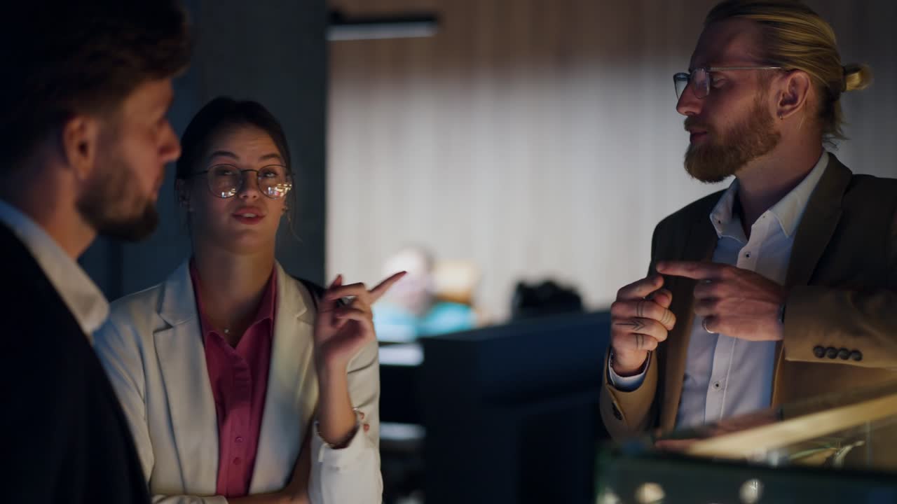 A trio of office workers stand near a shop window and communicate. Girl in a white business suit, light brown brunette guy talking in a modern office