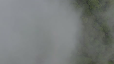 Aerial-top-down-of-clouds-passing,-revealing-curved-road-surrounded-by-green-dense-rainforest,-San-Luis-Morete,-Costa-Rica