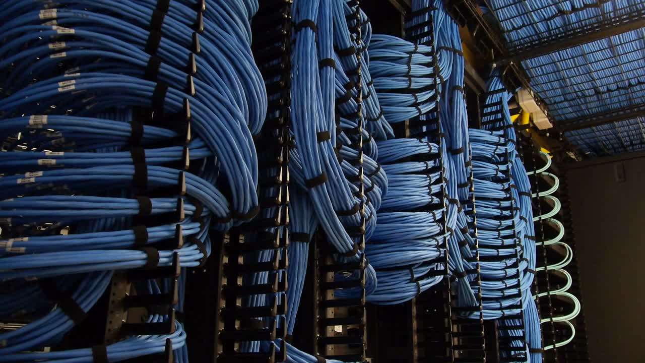 toma desde plataforma rodante que revela una gran red de cables azules entrelazados en una sala de servidores