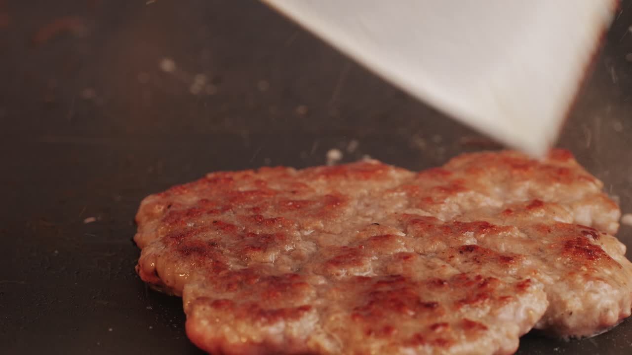Cooking American fat smash burger on grill close-up. Beef or pork cutlet smashing by burger press. The chef in kitchen of the restaurant making cutlets for burgers - smash burger beefsteak. Fast and street food concept. High quality 4k footage