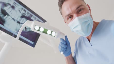 dentista caucásico con máscara facial examinando los dientes en una clínica dental moderna