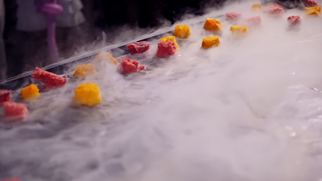 Cook chef is making fruit ice cream added liquid nitrogen. Cold dessert with thick white steam on the large surface with fruit for guests in the evening.