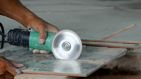 trabajador cortando una baldosa usando una molienda de ángulo en el sitio de construcción