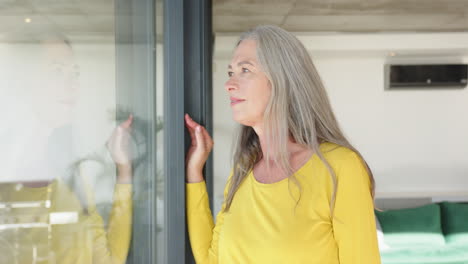 smiling woman in yellow shirt looking out window, enjoying peaceful moment at home