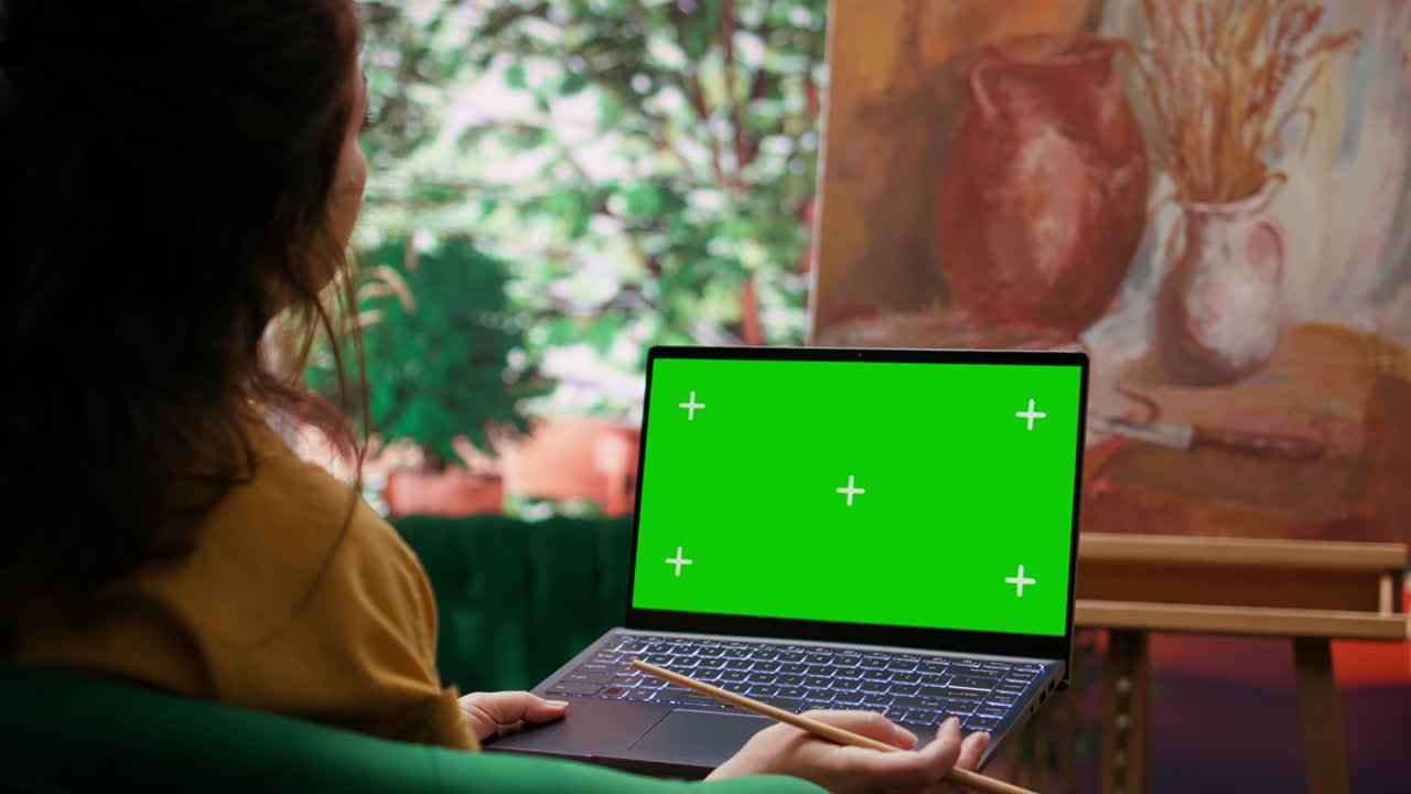 Woman using laptop with green screen while painting in art studio