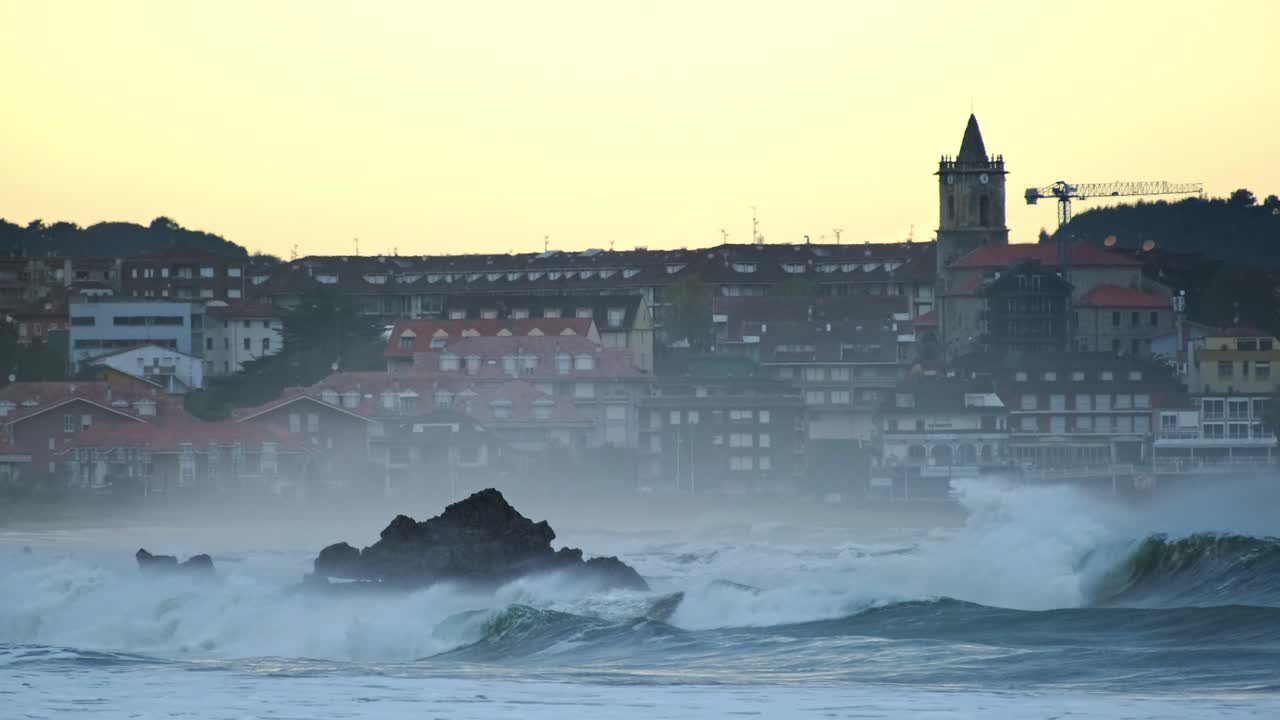 저녁에 도시 건물을 배경으로 바위 위로 부서지는 큰 파도