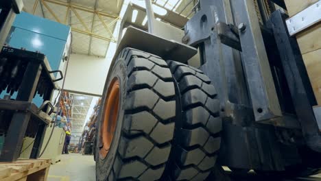 slow motion close-up shot of the moving wheels of a forklift that loads a wooden box inside an industrial warehouse and in the background you can see workers with helmets working