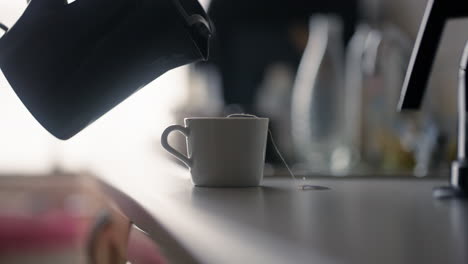 primer plano de una bolsa de té sumergida en una taza mientras se vierte agua caliente de una tetera