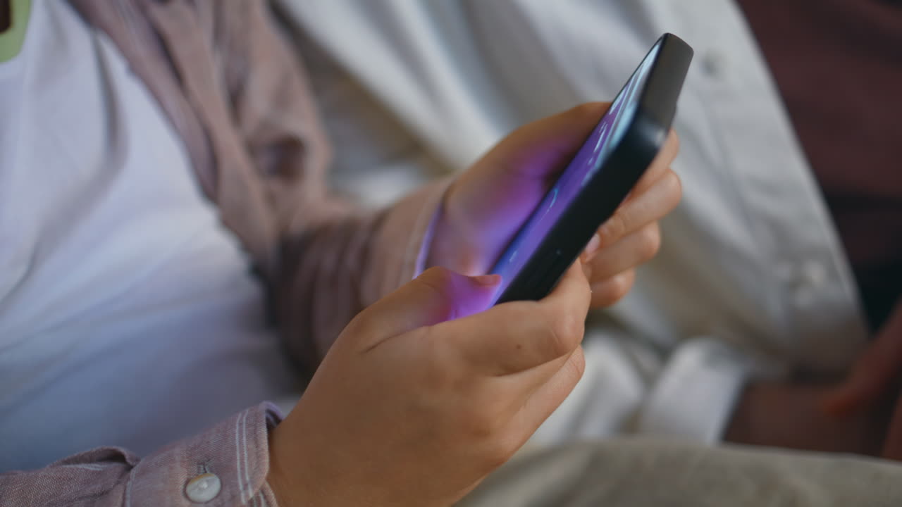 Child hands playing mobile phone at cozy sofa at evening closeup. Boy having fun