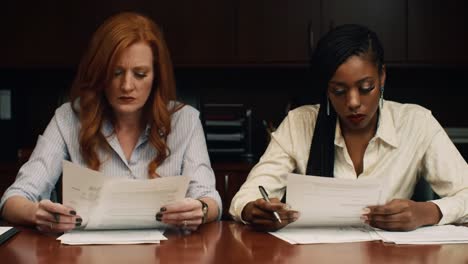 in a contemporary office, two women engage in focused discussions while reviewing important papers.