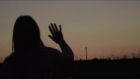 Alone-woman-silhouette-waving-goodbye-in-a-sunset