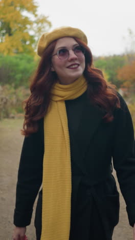 estudiante con una boina amarilla y gafas de sol camina a través de un hermoso jardín, tocando su cabello y ajustando sus gafas, rodeada de vibrante follaje de otoño