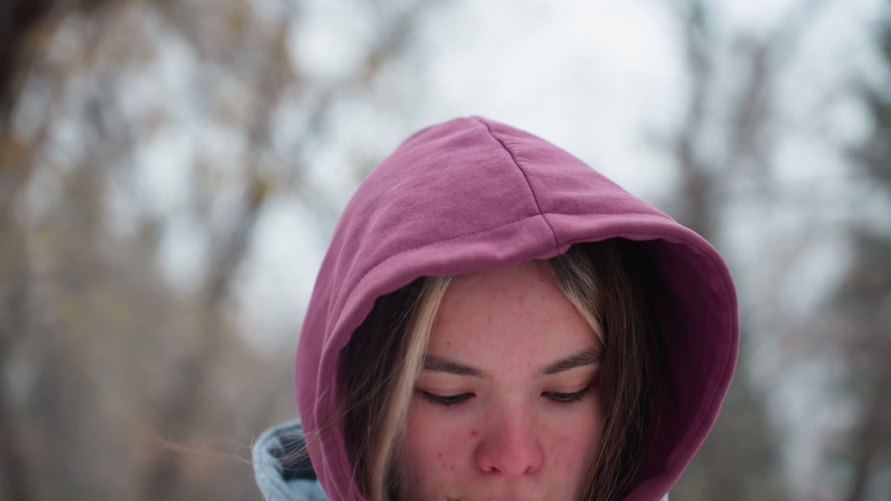 겨울에 야외에서 점프하는 여성의 클로즈업, 후드 재을 입고, 그녀는 나무와 자연의 흐릿한 눈 바탕에 추위에서 약간 은 얼굴을 가지고 있습니다.