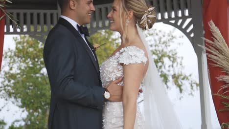 bride and groom stand tightly under gazebo