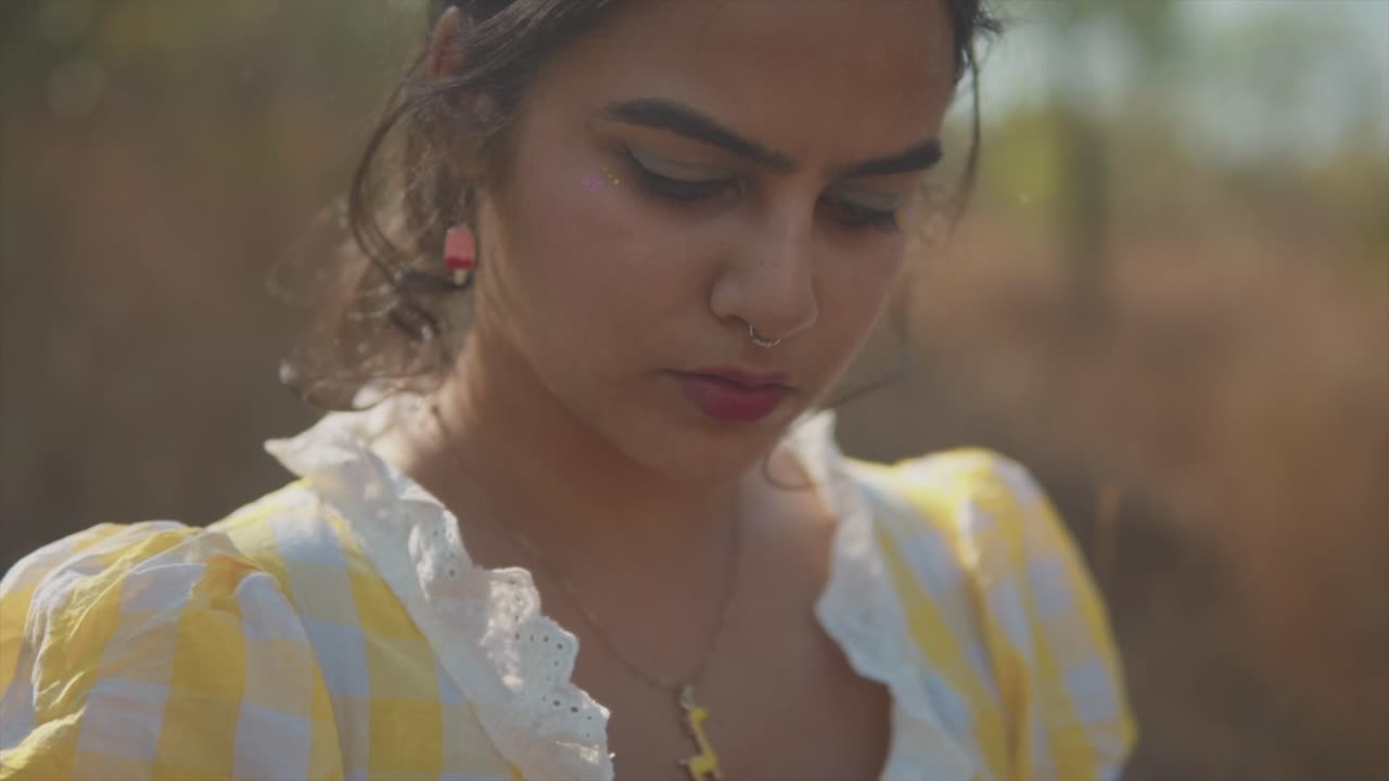 A close up shot of the face of an attractive Asian female glancing down, her hair fluttering in the morning breeze on a beautiful day outdoors, India