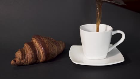 verter café de prensa francesa en una taza blanca junto a un croissant