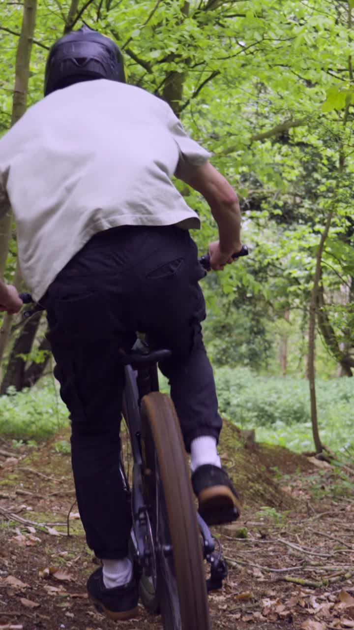 Drone Vertical Video Tracking Man On Mountain Bike Cycling Doing Mid-Air Jump On Trail Through Woodland 3