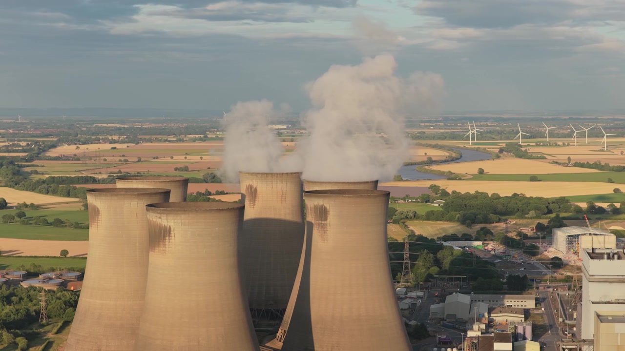 Grandi torri di raffreddamento industriali presso la centrale elettrica di Drax rilasciano nuvole di vapore nel cielo sereno sopra il paesaggio rurale del North Yorkshire durante una calda giornata estiva in Inghilterra.