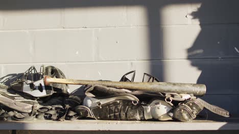 pile of protective baseball pads, helmets and a baseball bat in the changing room at baseball pitch